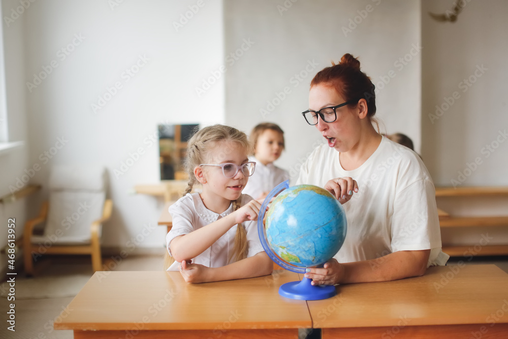 Fototapeta premium a teacher and a girl, a student, a child at school at a desk working with a globe, a teacher and a student are studying geography, looking for countries on the map. , modern education and technology