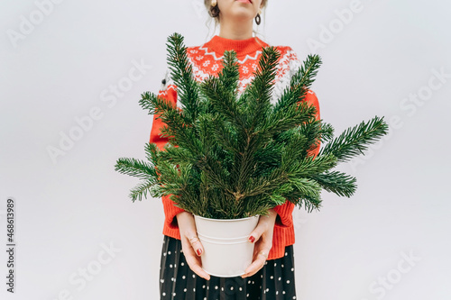 a modern woman in a red sweater with fir branches in her hands at Christmas on a light background. The minimum concept of the new year. no face