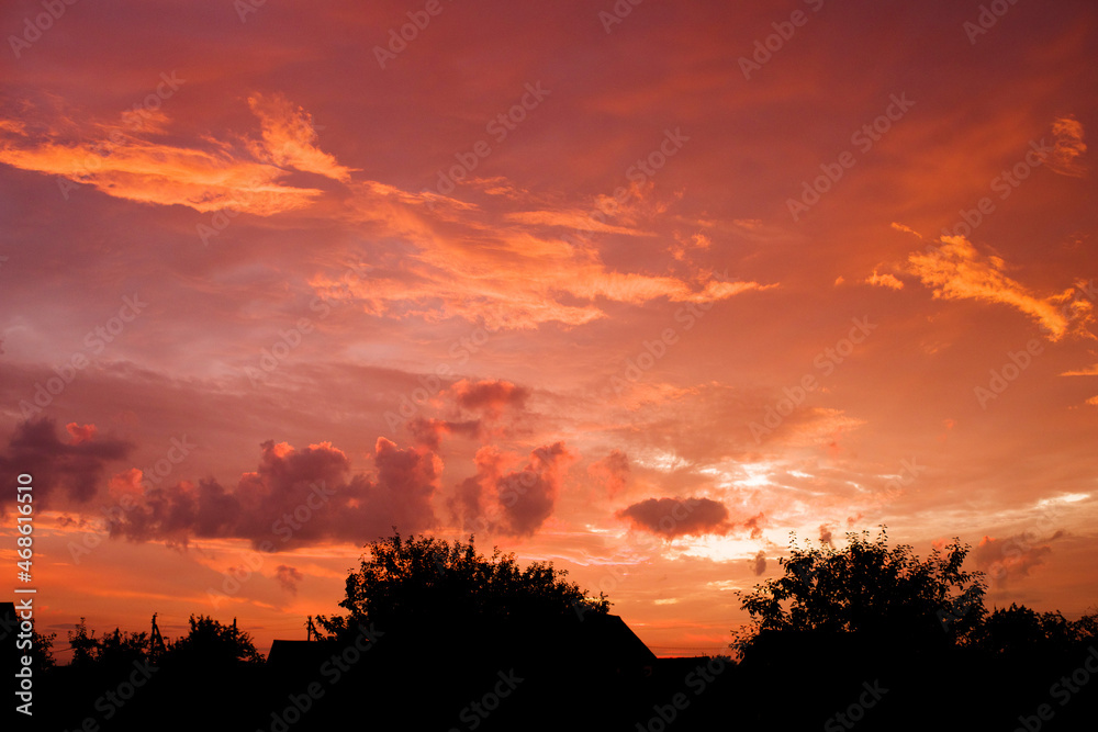Red and orange cloudy sky before sunrise against a black silhos of rustic roofs and trees. August Landscape with Dawn Sky Red and orange cloudy sky before sunrise against a black silhos of rustic roofs and trees. August Landscape with Dawn Sky