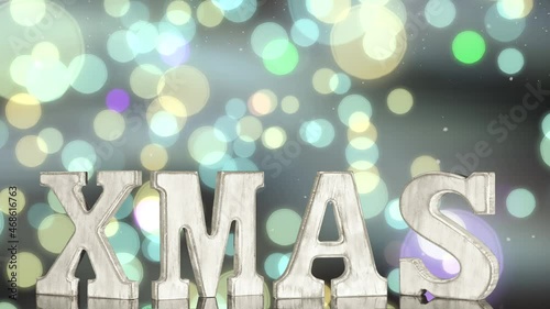 The letters XMAS rotate on a glowing colored bokeh background with floating snow particles