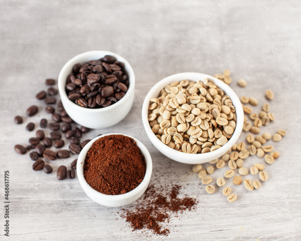 Green and brown unroasted and dark roasted coffee beans in white bowls Green and brown unroasted and dark roasted coffee beans in white bowls