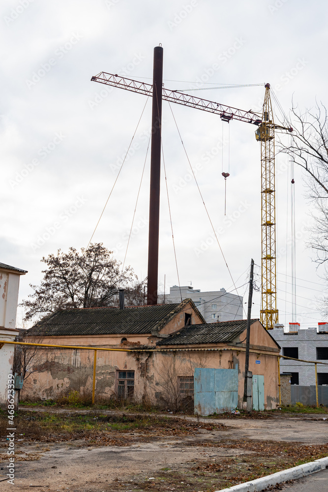 An old crumbling building, against the background of a new area under construction. A small boiler house is being destroyed, against the background of construction equipment and houses under construct An old crumbling building, against the background of a new area under construction. A small boiler house is being destroyed, against the background of construction equipment and houses under construct