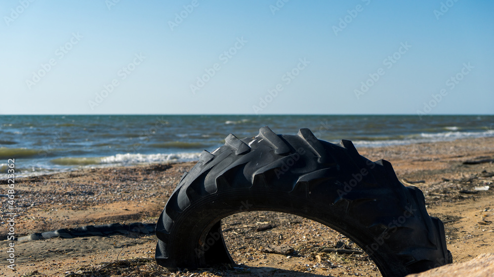 Fototapeta premium An image of an old car tire ingrown into the sand. Old car tire lying on the beach.
