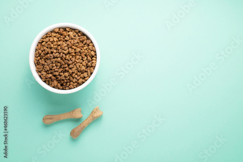A full bowl of dry pet food and natural toothpicks. On a colored background, top view, copy space.