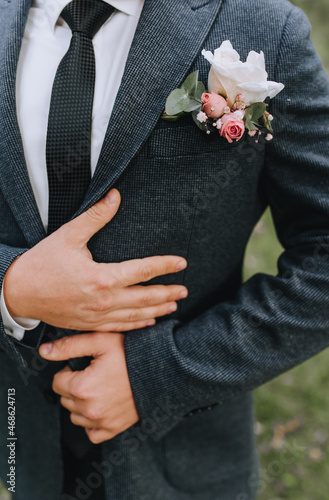 Wedding portrait of stylish groom in gray suit, white shirt, black tie and boutonniere outdoors.