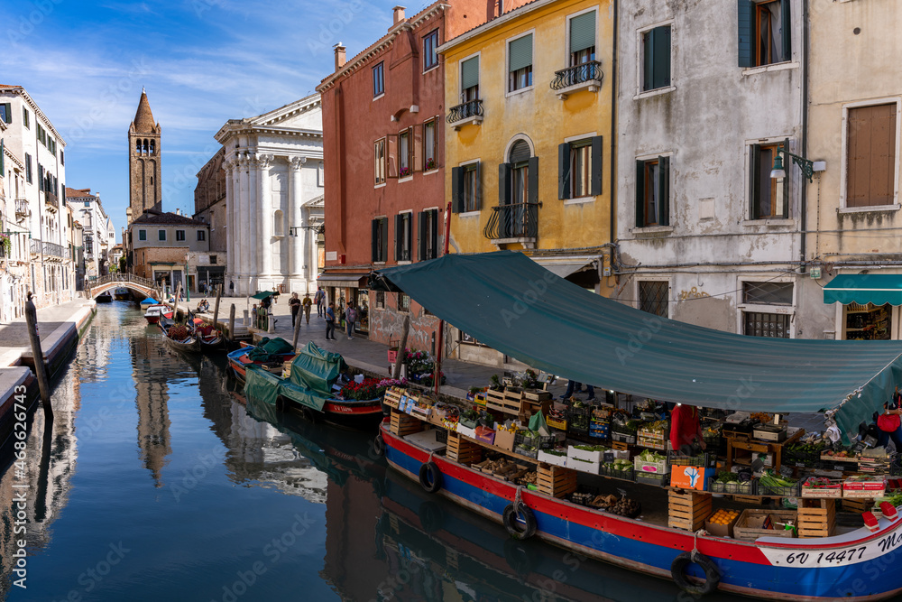 view of the canals of Venice with church and a grocery store on a boat in the foreground