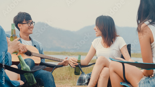 Group of Asia best friends teenagers drink beer chill dance enjoy guitar music with happy moments together beside tents in national park camp. On the background beautiful nature, mountains and lake.