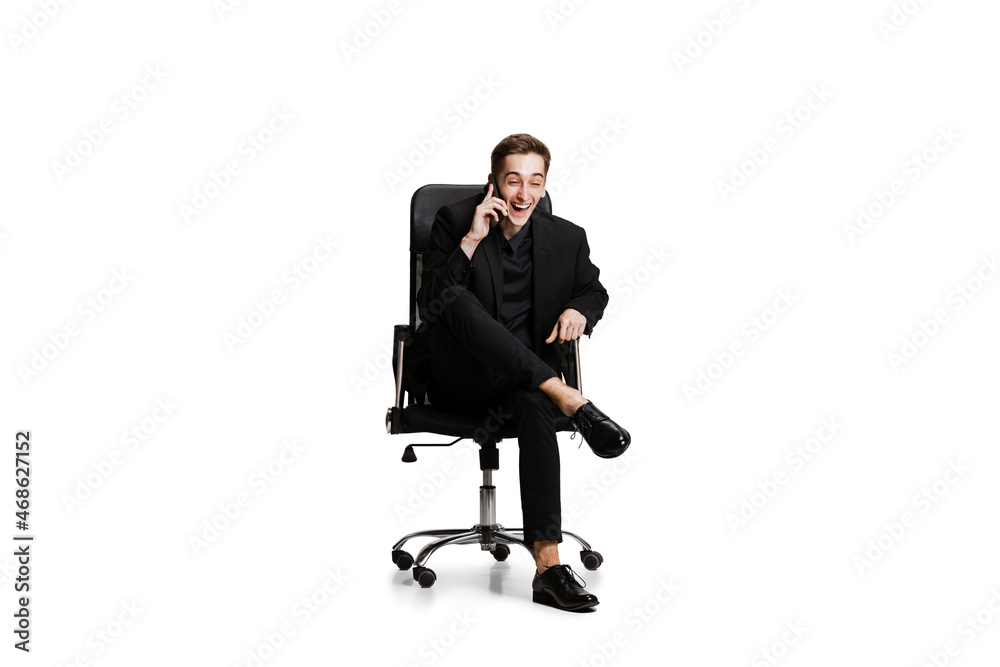 Portrait of young man in black business suit, office manager sitting on chair isolated on white background. Art, inspiration concept. Portrait of young man in black business suit, office manager sitting on chair isolated on white background. Art, inspiration concept.