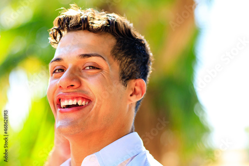 Handsome man in white shirt with show-white smile looking at camera in summer park