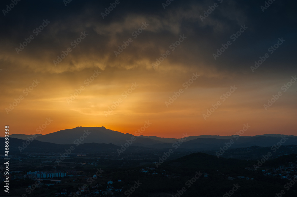 A silhouette of a mountain against a sunset sky