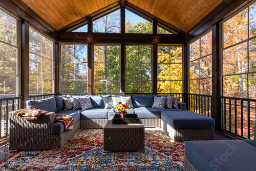 Cozy screened porch with contemporary furniture and flower bouquet in a vase, autumn leaves and woods in the background.