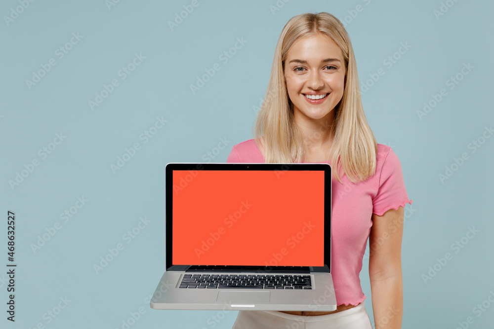 Naklejka premium Young smiling happy caucasian blonde woman 20s wear casual pink t-shirt hold use work on laptop pc computer blank screen workspace area isolated on plain pastel light blue background studio portrait