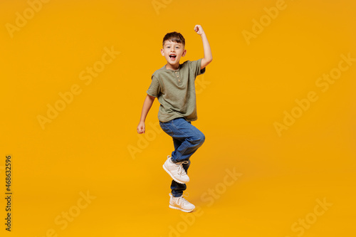 Full body little small fun happy boy 6-7 years old wearing green t-shirt do winner gesture clench fist isolated on plain yellow background studio portrait. Mother's Day love family lifestyle concept. photo