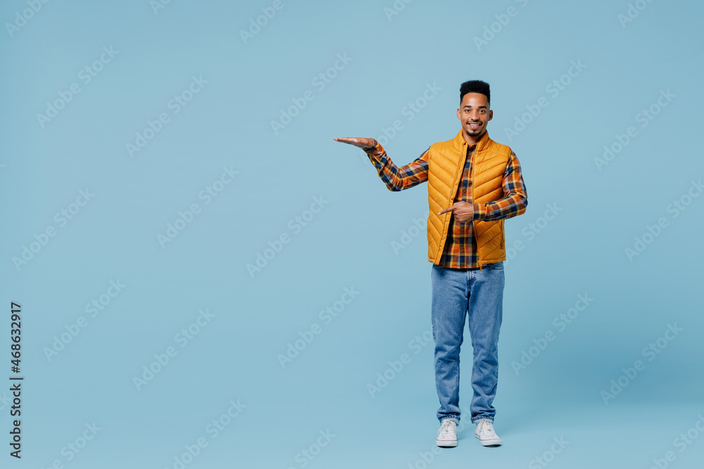 Full size body length fun young black man 20s years old wear yellow waistcoat shirt pointing on lower palm with copy space place mock up isolated on plain pastel light blue background studio portrait Full size body length fun young black man 20s years old wear yellow waistcoat shirt pointing on lower palm with copy space place mock up isolated on plain pastel light blue background studio portrait