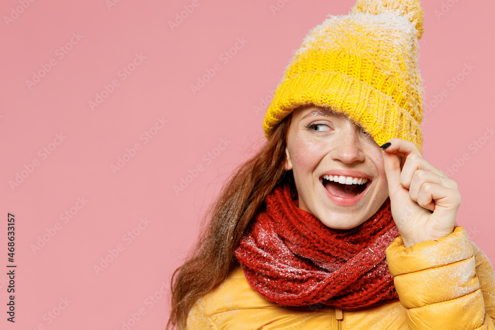 Joung woman 20s years old wears yellow jacket hat mittens look aside pull cap with hand cover close hiding eye with hat keep mouth open isolated on plain pastel light pink background studio portrait. Joung woman 20s years old wears yellow jacket hat mittens look aside pull cap with hand cover close hiding eye with hat keep mouth open isolated on plain pastel light pink background studio portrait.