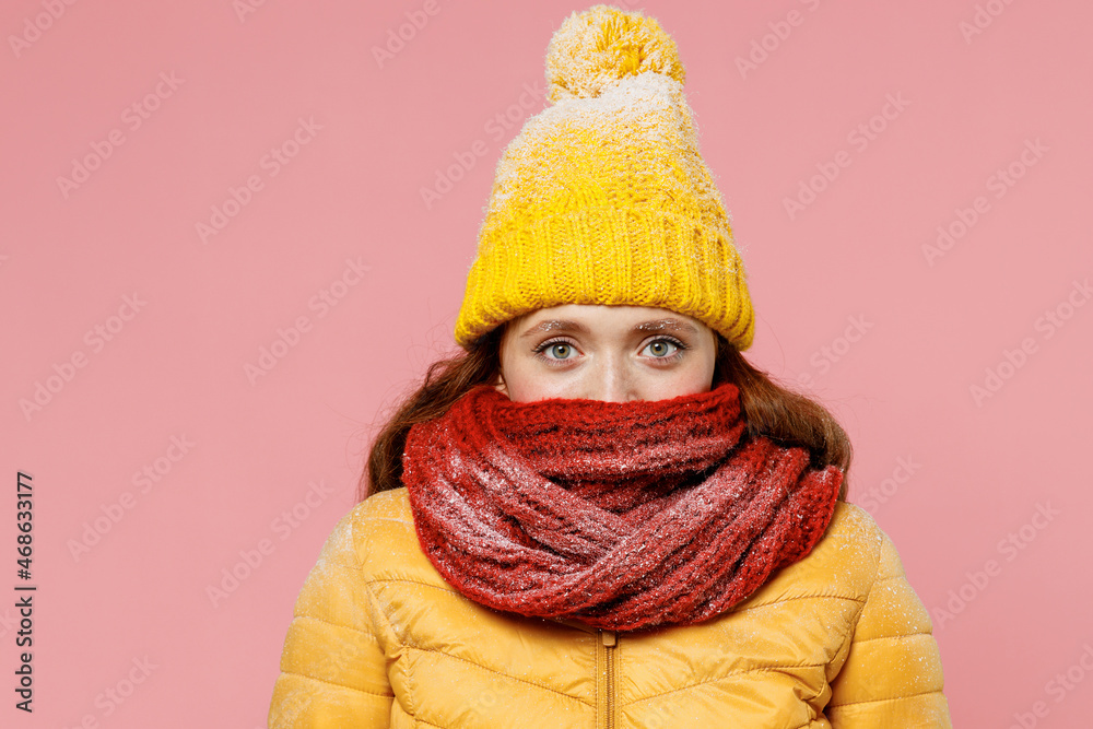 Charming young woman 20s years old wear yellow jacket hat mittens looking camera cover close hiding mouth with scarf wrapped around neck isolated on plain pastel light pink background studio portrait