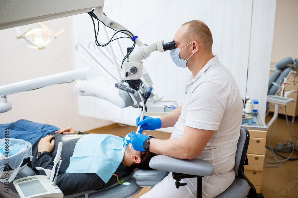 The dentist treats his patient's teeth with a microscope. The dentist treats the patient's mouth. Dental care The dentist treats his patient's teeth with a microscope. The dentist treats the patient's mouth. Dental care