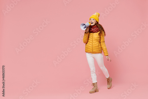 Full size body length promoter young woman 20s wear yellow jacket hat mittens hold scream in megaphone announces discounts sale Hurry up isolated on plain pastel light pink background studio portrait