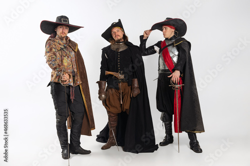 Full-length portrait of thee men in vitage costumes with swords, musketeer and pirate isolated over white background photo