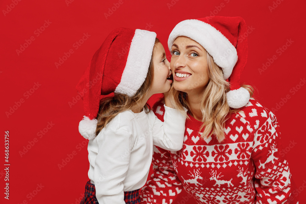 Young woman wear sweater have fun with child baby girl 6-7 years old Mommy little kid daughter whisper gossip tells secret isolated on plain red color background studio. New Year love family concept. Young woman wear sweater have fun with child baby girl 6-7 years old Mommy little kid daughter whisper gossip tells secret isolated on plain red color background studio. New Year love family concept.
