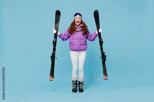 Full body skier shocked happy cheerful fun woman in warm purple padded windbreaker jacket goggles mask spend extreme weekend in mountains hld ski look camera isolated on plain blue background studio photo