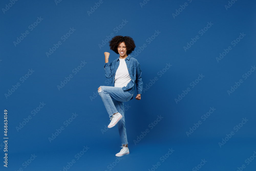 Full body young smiling happy black woman in casual clothes shirt white tshirt do winner gesture clench fist celebrate isolated on plain dark blue background studio portrait. People lifestyle concept