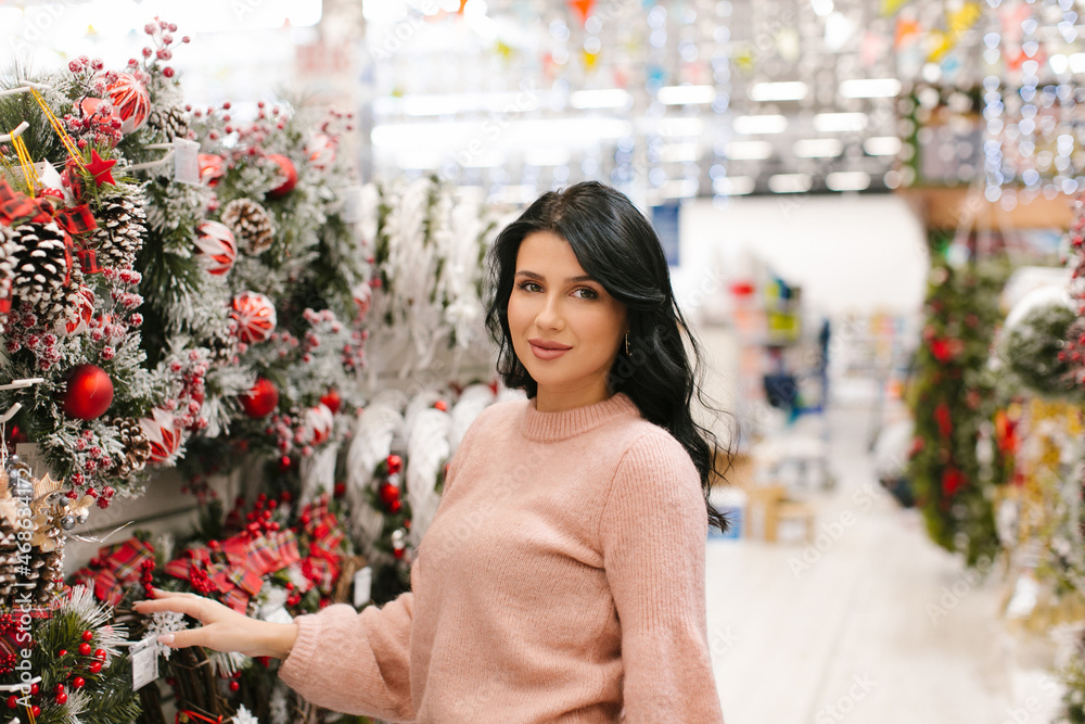 Young brunette woman in a pink sweater chooses a Christmas wreath in the store. New Year's shopping. Young brunette woman in a pink sweater chooses a Christmas wreath in the store. New Year's shopping.