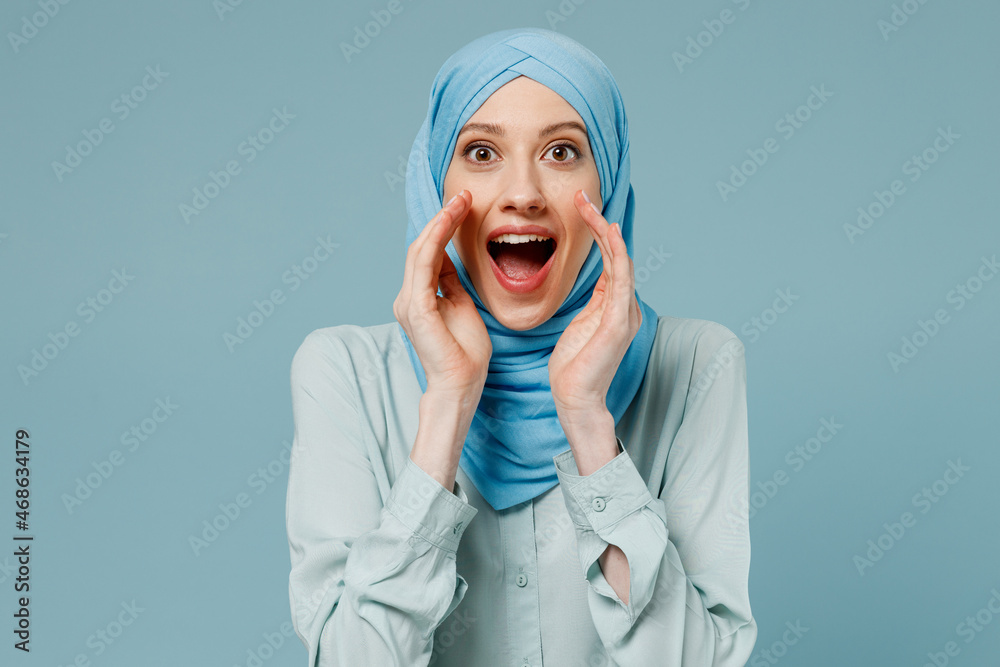Young arabian asian muslim woman in abaya hijab scream hot news about sales discount with hands near mouth isolated on plain blue background studio. People uae middle eastern islam religious concept. Young arabian asian muslim woman in abaya hijab scream hot news about sales discount with hands near mouth isolated on plain blue background studio. People uae middle eastern islam religious concept.