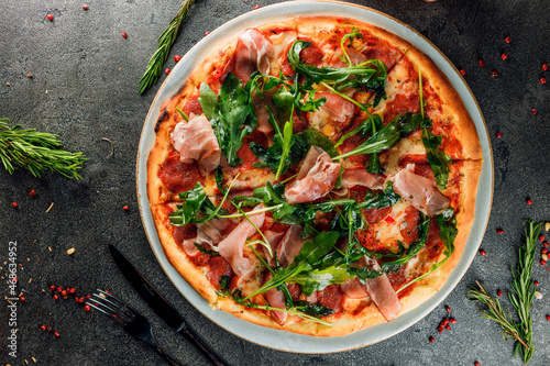 pizza with ham, salami and arugula on a dark background. top view