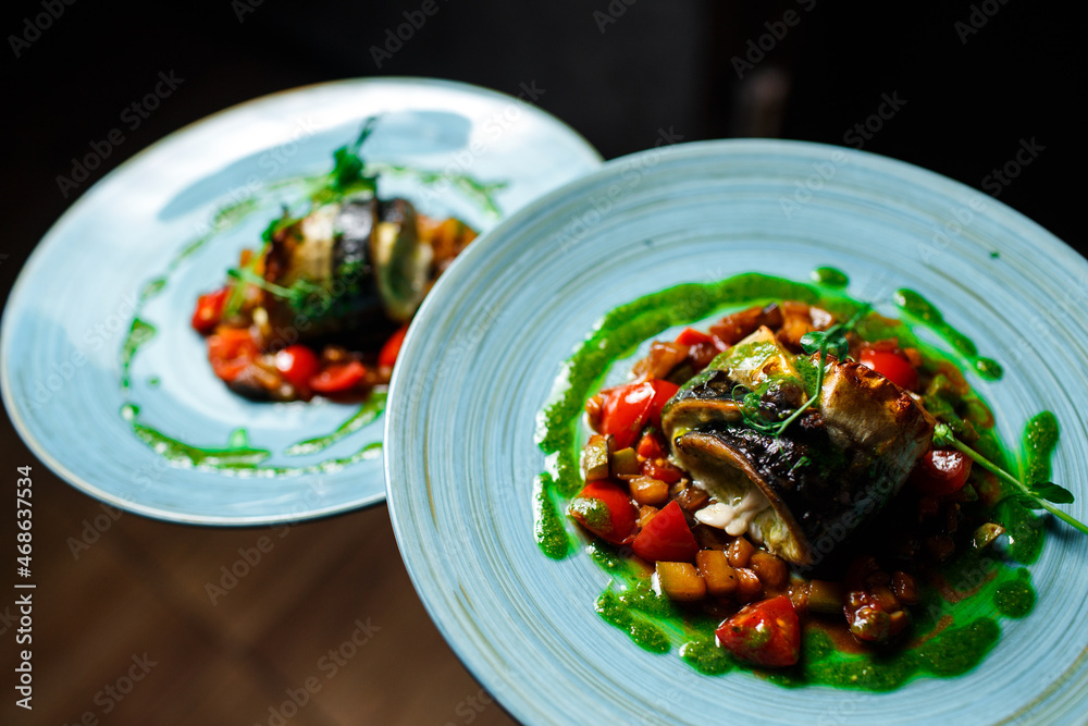 Fish dish - roasted fish and vegetables on a blue plate on a dark background Fish dish - roasted fish and vegetables on a blue plate on a dark background