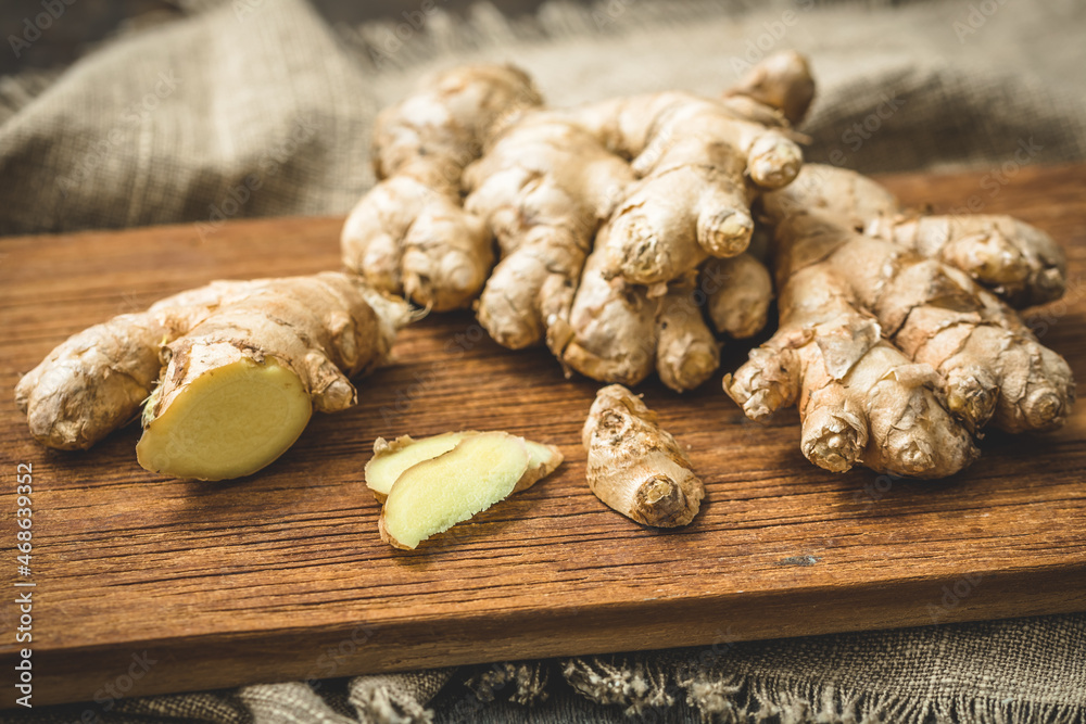 Fresh ginger on a wooden board, whole roots and cut slices