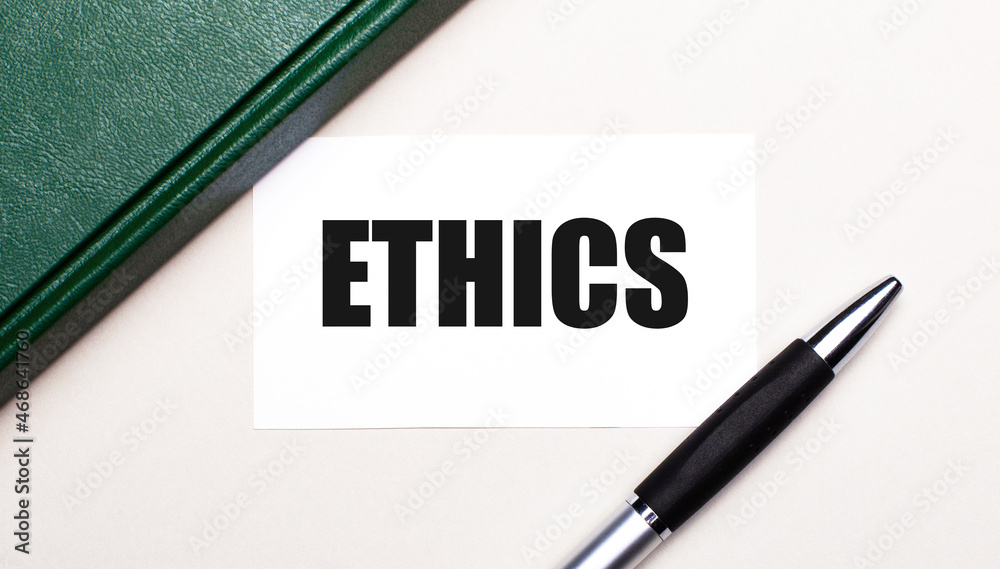 On a light gray background lies a pen, a green notebook and a white card with the text ETHICS. Business concept.