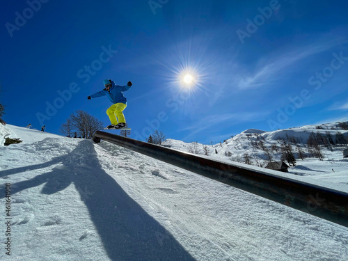 LENS FLARE: Athletic snowboarder does a railslide trick while riding in fun park photo