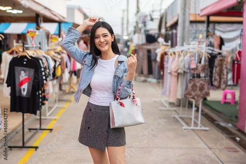 Beautiful asian female young model lady having a solo shopping and stroll walk time by herself and looking through concentratedly some fashion dresses put on sale at a fashion store in a night market 