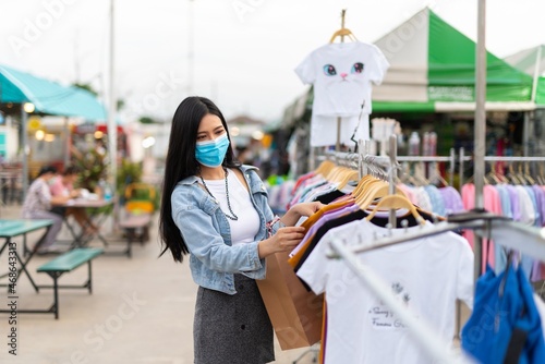 Beautiful asian female young model lady wearing mask having a solo shopping by herself and looking through concentratedly some fashion product put on sale at a fashion store in a night market 