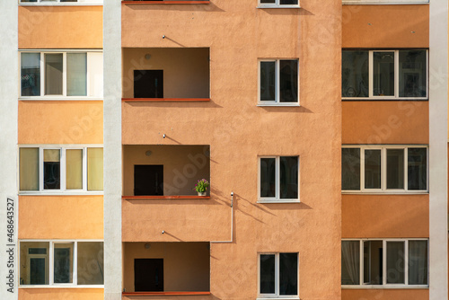 Petunia flower pot on a balcony in sunlight on the yellow wall of an apartment building. Reflections in the windows on the facade of the house