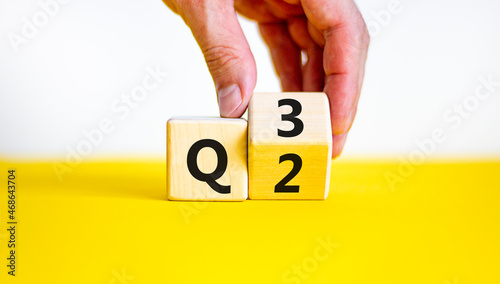 From 2nd to 3rd quarter symbol. Businessman turns a wooden cube and changes words 'Q2' to 'Q3'. Beautiful yellow table, white background. Business, happy 3rd quarter Q3 concept, copy space. photo