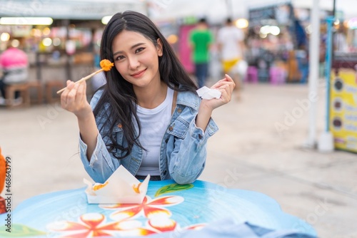 Beautiful asian female young model lady having a stroll walk relaxingly and eating delicious and tasty street food from the food bazaar in a night market happily and cheerfully