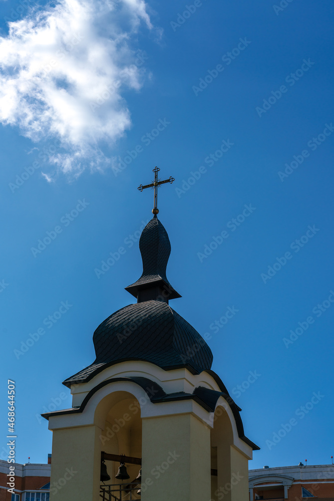 Rays of sunlight fall on the bells and cross of the bell tower under a blue sky with a lonely white cloud Rays of sunlight fall on the bells and cross of the bell tower under a blue sky with a lonely white cloud