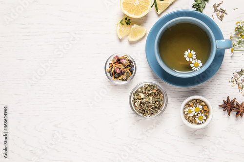 Flat lay composition of freshly brewed tea with chamomile flowers and dry leaves on white wooden table. Space for text