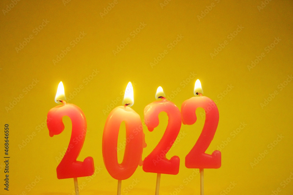 The 2022 numbers are on a yellow background. Pink Christmas candles 2022. Candles burn with lights. Insulated. New Year. Christmas. Copy space The 2022 numbers are on a yellow background. Pink Christmas candles 2022. Candles burn with lights. Insulated. New Year. Christmas. Copy space