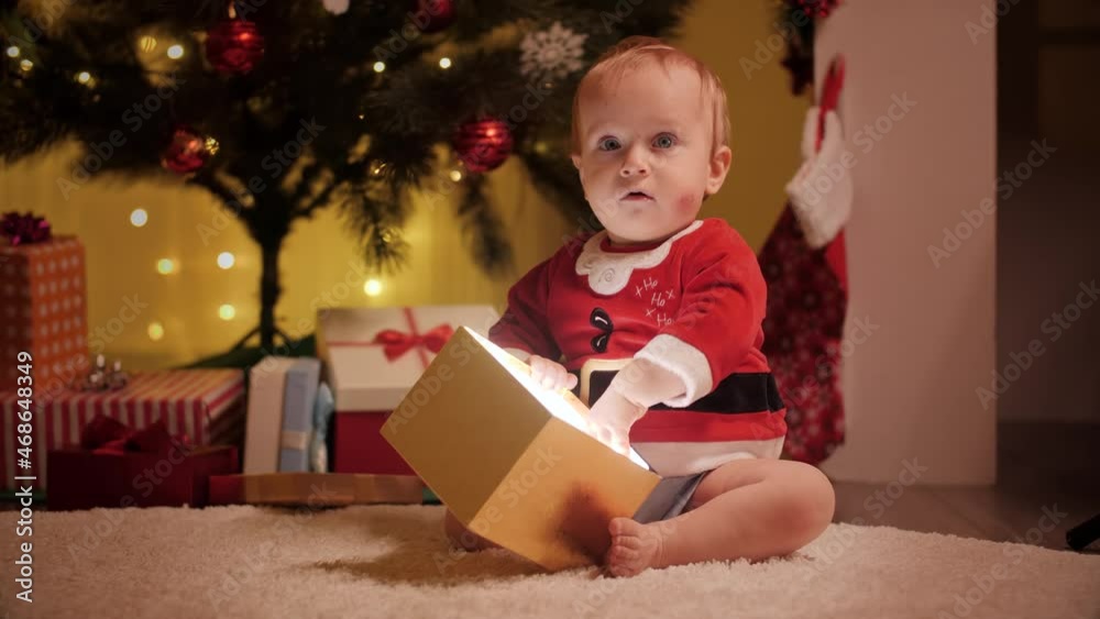 Cute baby boy in Santa costume looking inside Christmas present box. Families and children celebrating winter holidays. Cute baby boy in Santa costume looking inside Christmas present box. Families and children celebrating winter holidays.