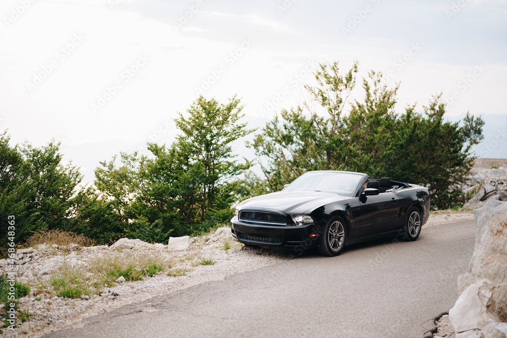 A black convertible car stands on a picturesque road in the mountains among the greenery 