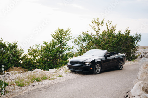 A black convertible car stands on a picturesque road in the mountains among the greenery  © Nadtochiy
