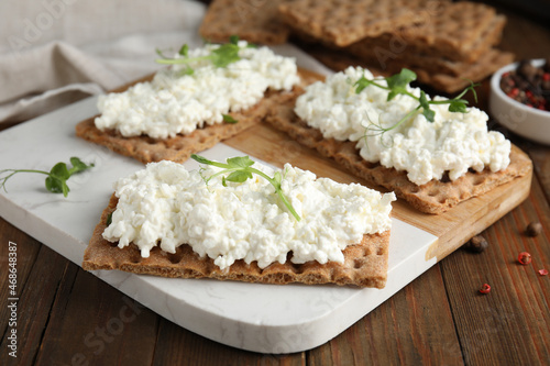 Crispy crackers with cottage cheese and microgreens on wooden table, closeup