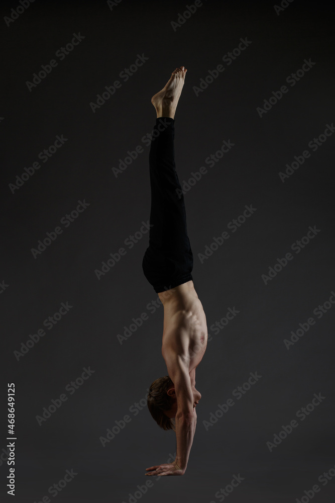 Athletic young guy performs a handstand isolated on a dark background.