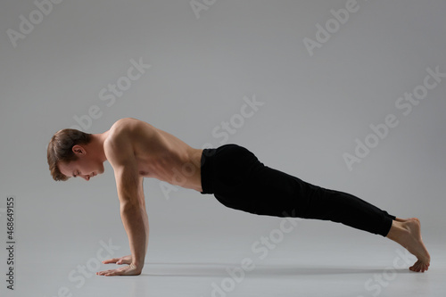 Athletic young guy performs plank exercise isolated on gray background.