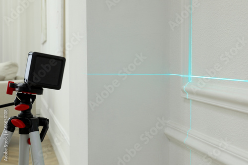 Cross line laser level on tripod in front of white wall © New Africa