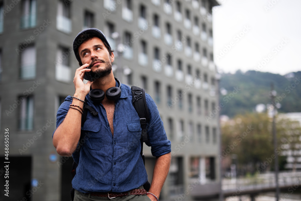 Young stylish man using the phone outdoors. Fashion happy man talking to the phone