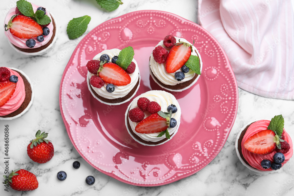 Delicious cupcakes with cream and berries on white marble table, flat lay